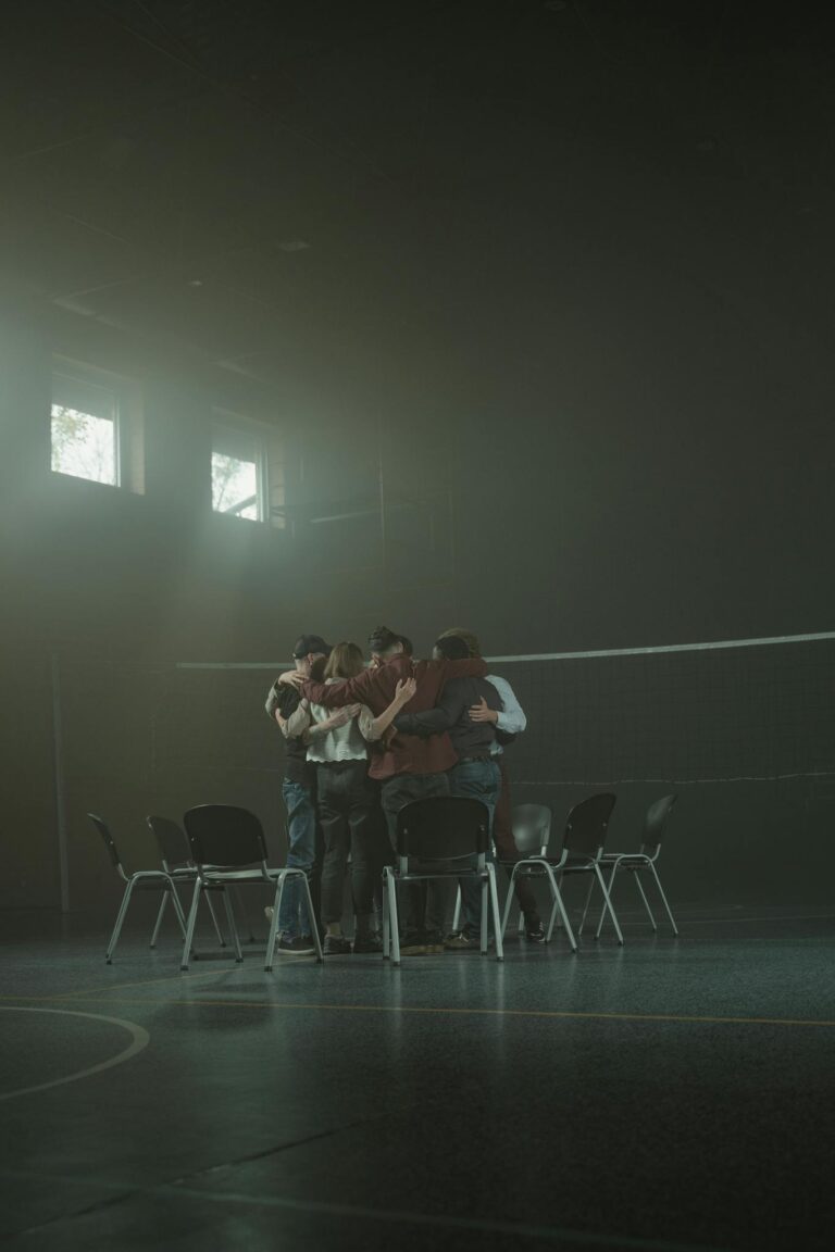 A diverse support group hugs in a dimly lit room, fostering unity and emotional support.